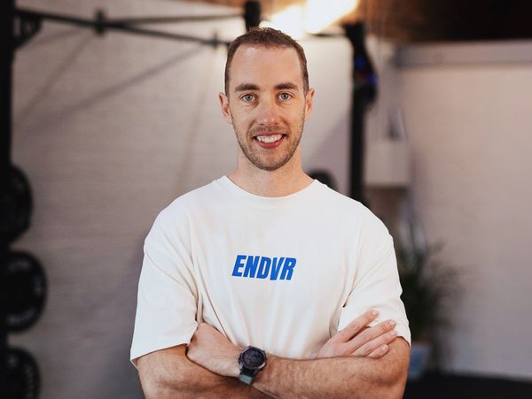 Smiling man wearing a white ENDVR t-shirt standing with arms crossed.