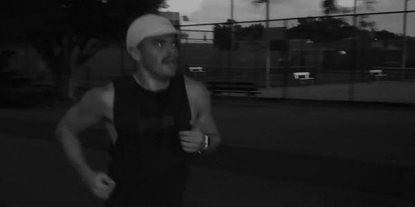 Man jogging outdoors at dusk wearing a cap and athletic gear.