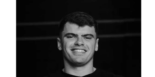 Smiling young man in a black shirt against a dark background.