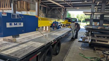 Worker securing equipment on a flatbed truck inside a warehouse.