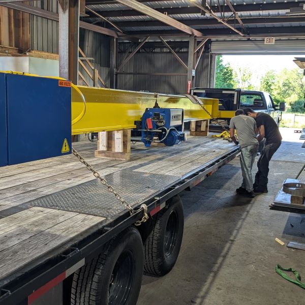 Two men inspecting machinery on a flatbed trailer inside a warehouse.