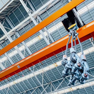 Industrial crane hooks hanging from an orange overhead beam in a warehouse.