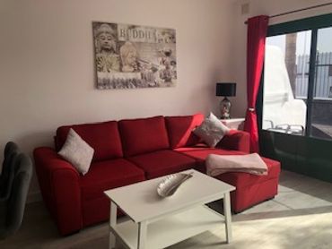 Sala acogedora con sofá rojo y mesa blanca.