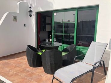 Patio con mesa y sillas negras y una tumbona blanca.