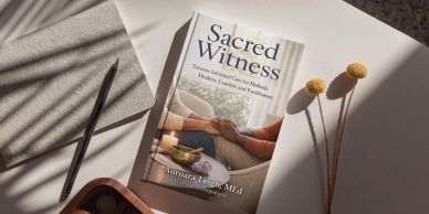 A book titled Sacred Witness lies on a white surface.