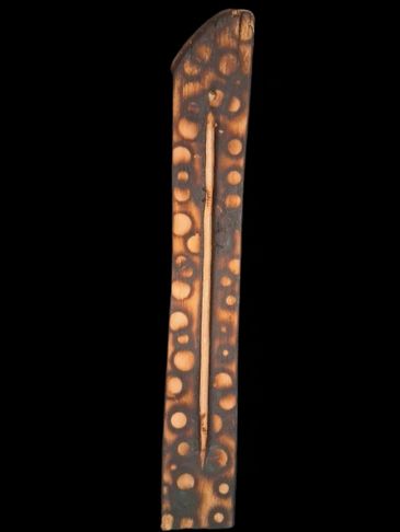 Long, rectangular wooden object with circular patterns.