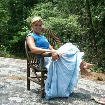 Woman in blue dress sitting on a wooden chair outdoors.