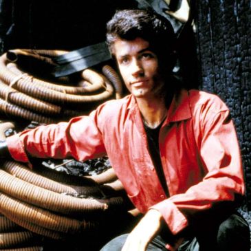 Young man in a red shirt sitting by coiled hoses.