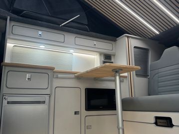 Compact kitchenette inside a camper van with fold-out table and storage cabinets.