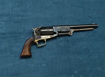 A vintage revolver with a wooden grip on a blue fabric background.