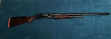 A classic wooden shotgun with a long barrel on a blue surface.