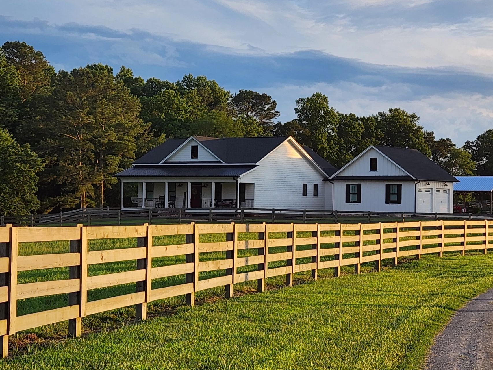 A country home with white fences and barns under a blue sky.