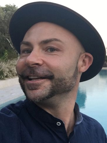 Man with a unique beard style wearing a black hat near a pool.