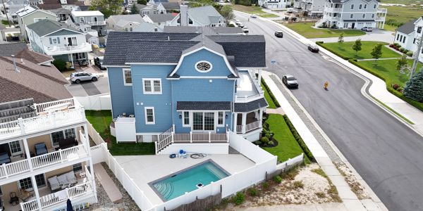 A blue house with a fenced pool near a sandy area and paved road.