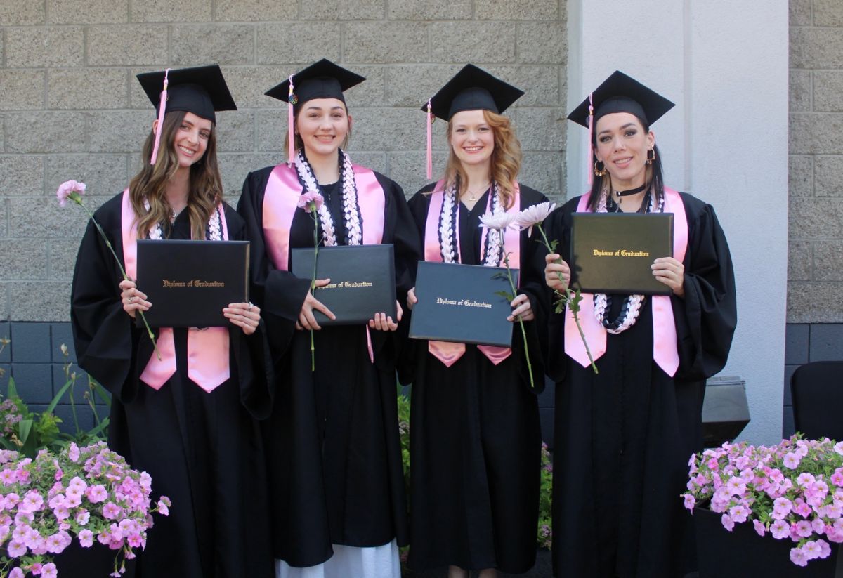 Massage Life Academy's first four graduates holding their diplomas outside the school