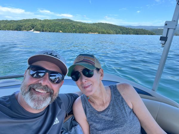 Smiling couple on a boat with a lake and green hills background.