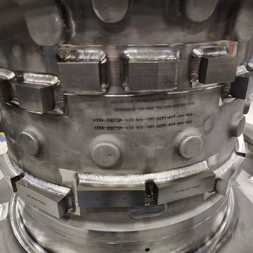 Close-up of a metallic industrial component with detailed welds and markings.