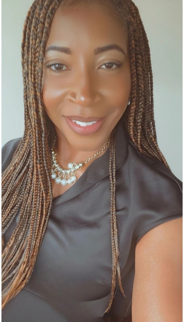 Smiling woman with braided hair wearing a pearl necklace and black top.
