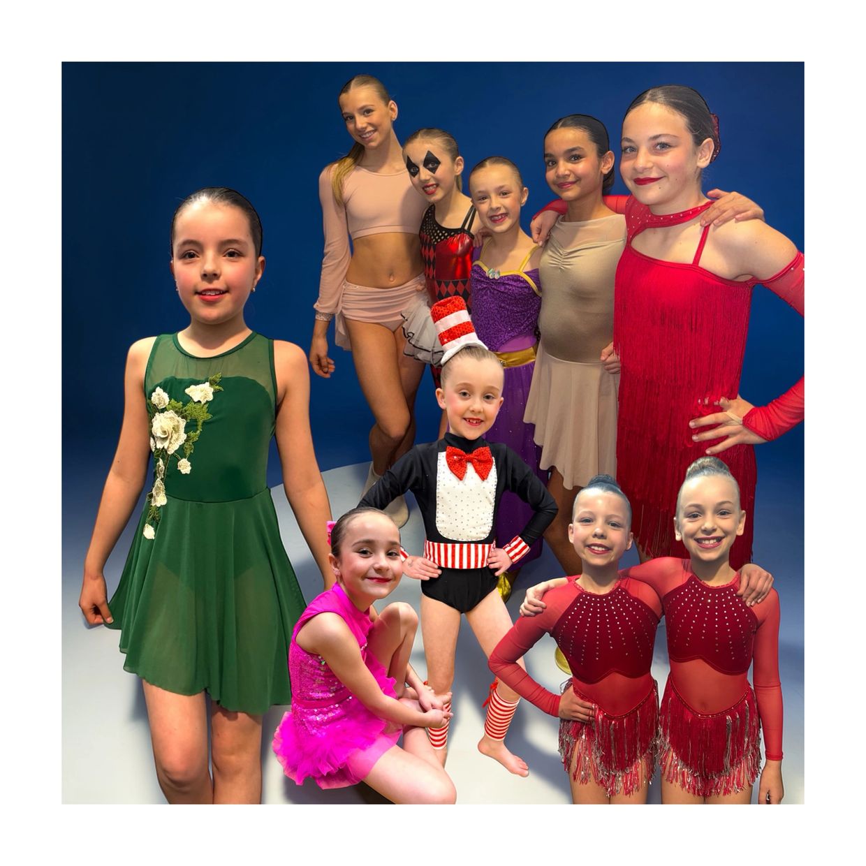 Young dancers in colorful costumes posing against a blue backdrop.