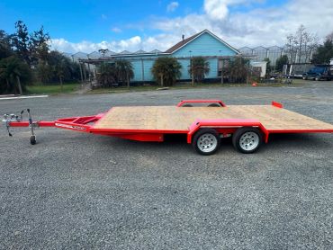 Red flatbed trailer parked on gravel.