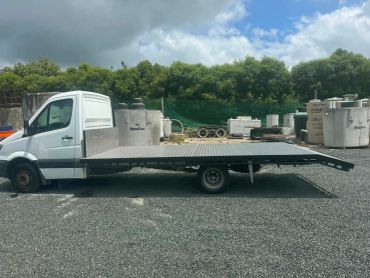 Flatbed truck with an extended ramp parked on gravel.