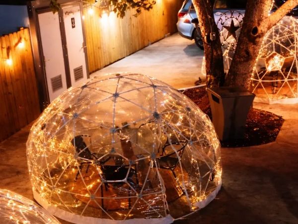 Outdoor dining domes decorated with string lights at night.