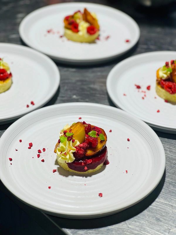 Elegant dessert with cream, raspberries, and caramelized fruit on white plates.