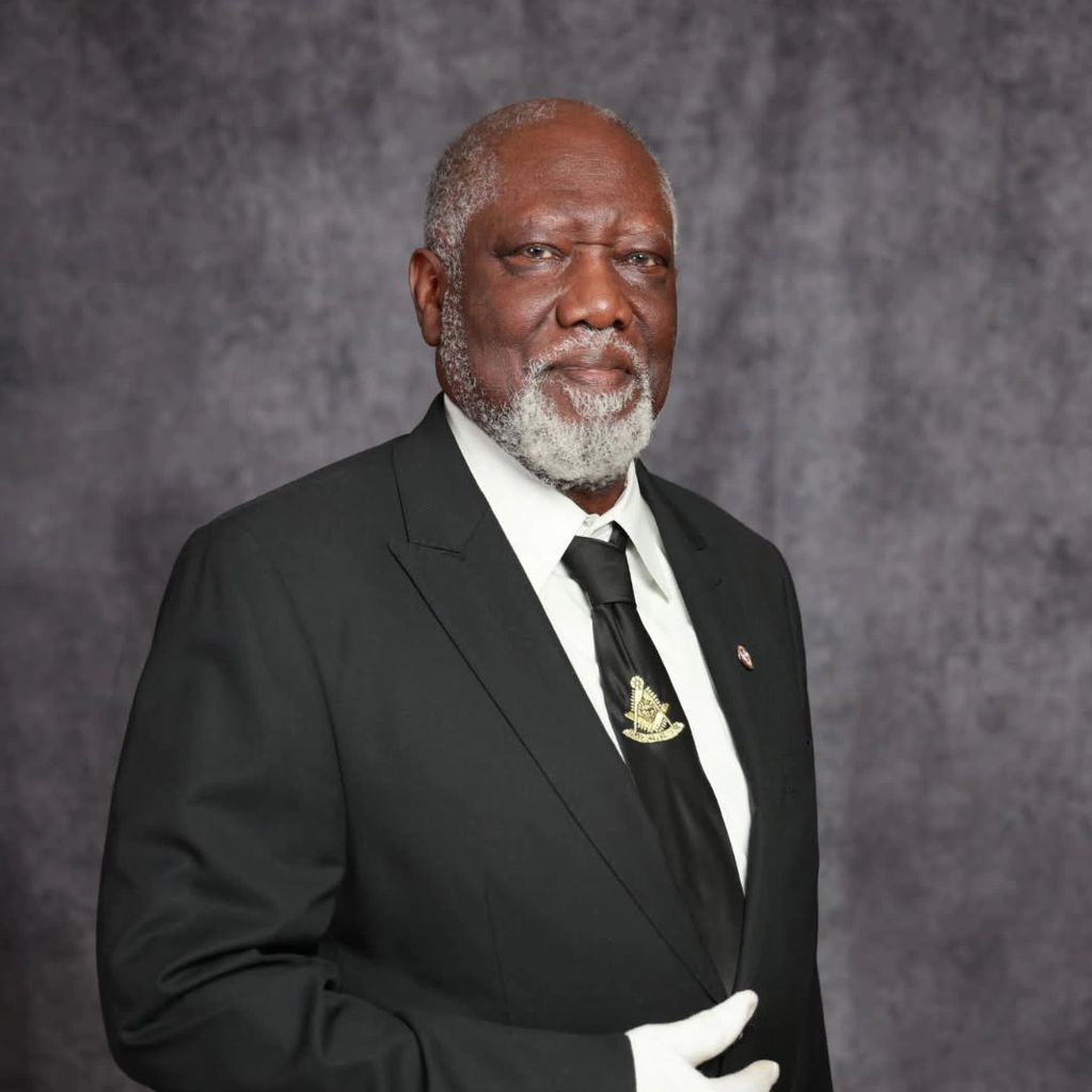 Elderly man in a black suit with a white beard and gloves.