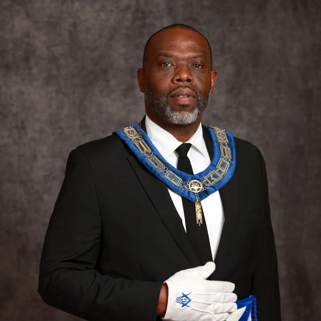 Man in formal attire wearing Masonic regalia with a white glove.