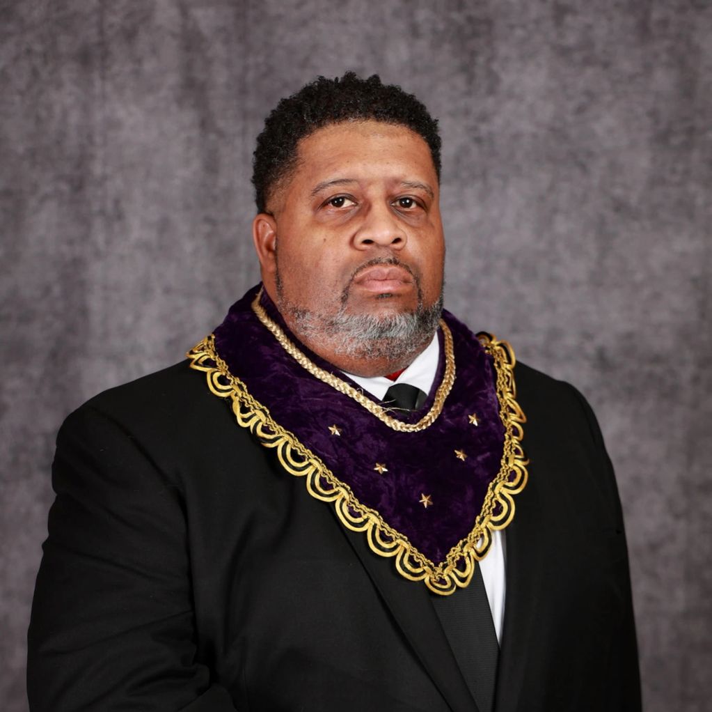 Man in formal attire with a purple and gold ceremonial collar.
