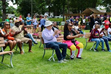 People sitting on benches outdoors, clapping and enjoying an event.