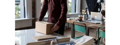 Person packing a cardboard box on a table in a bright office.