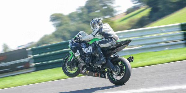 Motorcyclist performing a wheelie on a racetrack in full gear.