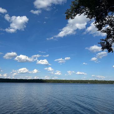 Peaceful lake under a bright blue sky with scattered clouds.