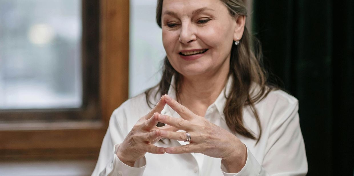 Smiling woman in white shirt with hands clasped thoughtfully.