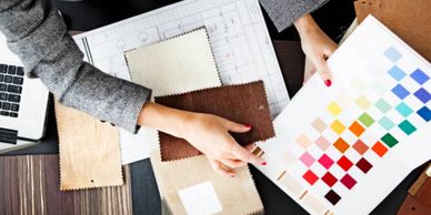 image of desk seen from above, with a person's arms holding a color chart and other paperwork