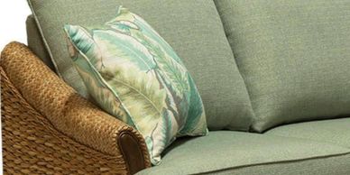 brown wicker couch, with green pillows and a patterned throw pillow