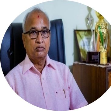 Elderly man sitting in an office chair, wearing glasses and a pink shirt.