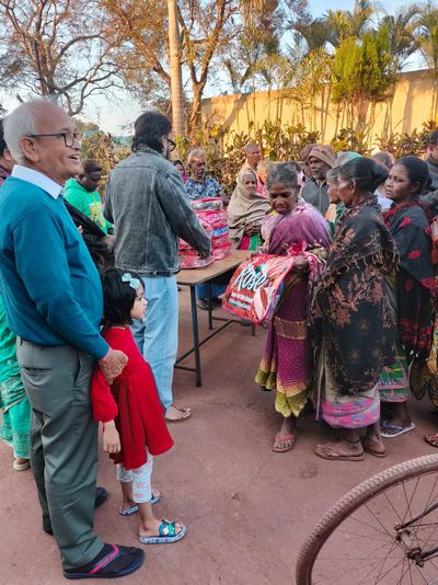 Volunteers distributing blankets to a group of people outdoors in a sunny setting.