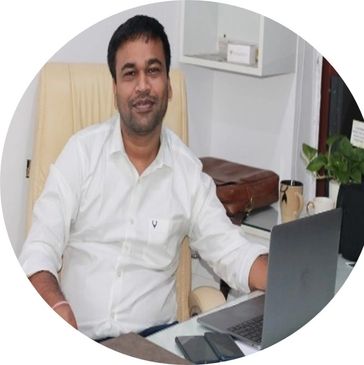Man in white shirt sitting at an office desk with a laptop and phone.
