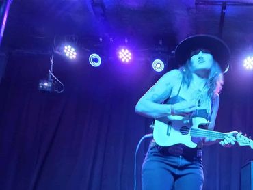 Musician playing an electric guitar under blue stage lights.