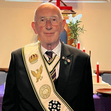 Elderly man in ceremonial attire with sash and pins.