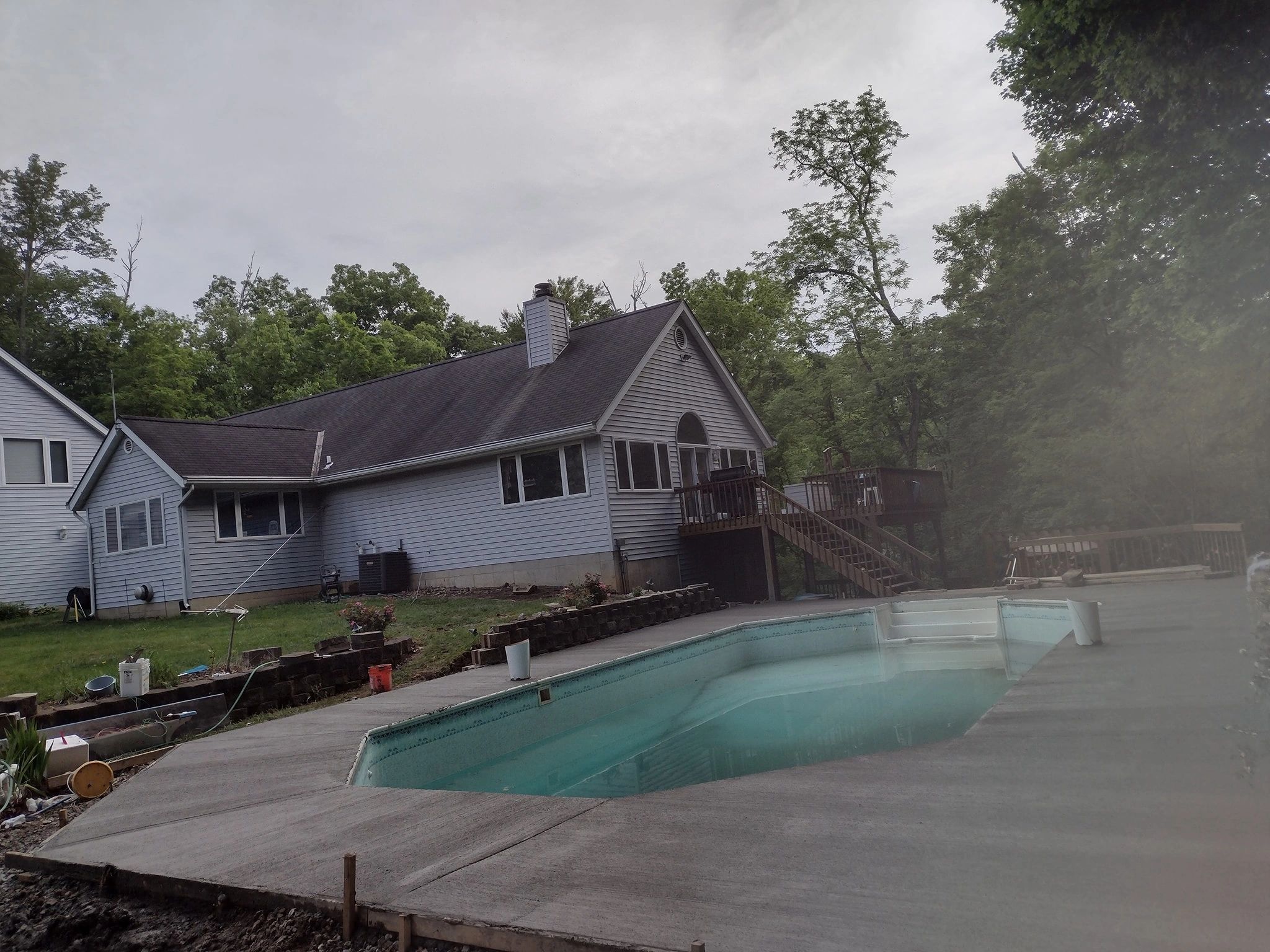 House with pool under cloudy sky and surrounding trees.