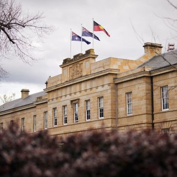 Historic building with three flags on top under cloudy sky.