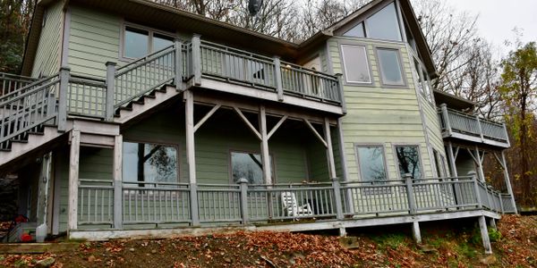 Green two-story house with wooden balconies surrounded by autumn trees.
