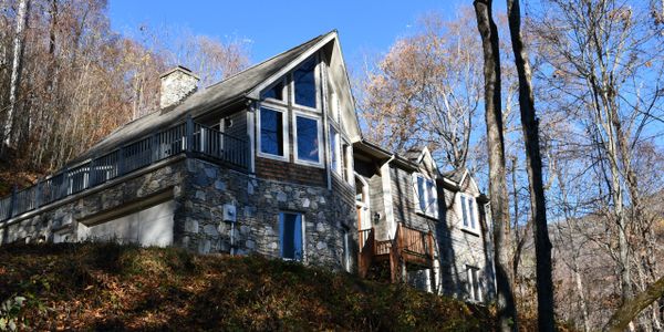 Stone and wood house on a hillside surrounded by trees under a clear blue sky.