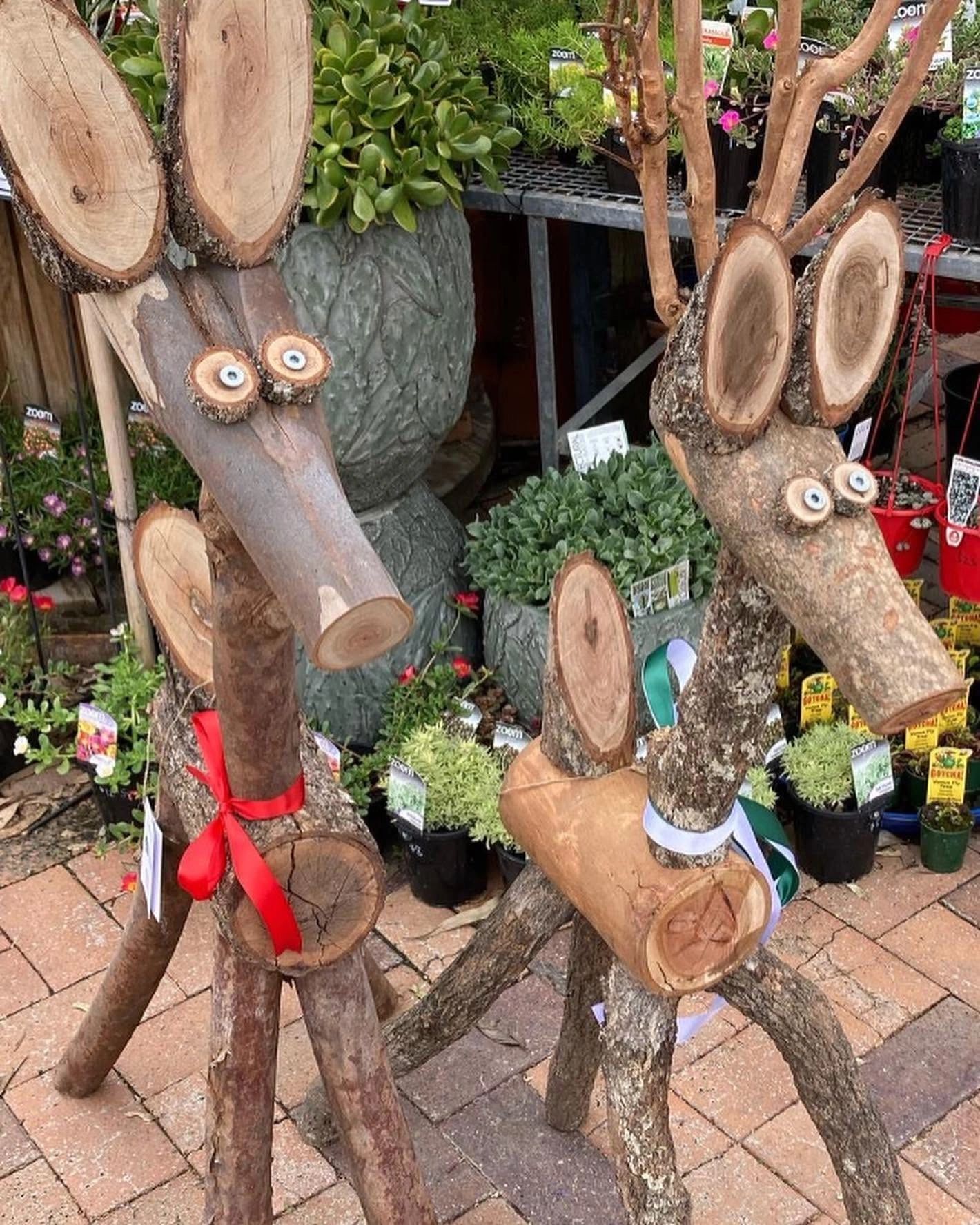 Wooden deer sculptures with ribbons at a garden center.