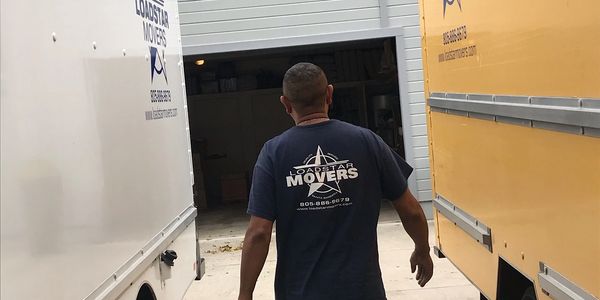Mover walking between two Loadstar Movers trucks toward a garage.