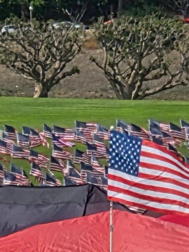 American flags displayed on a field with tents in foreground.