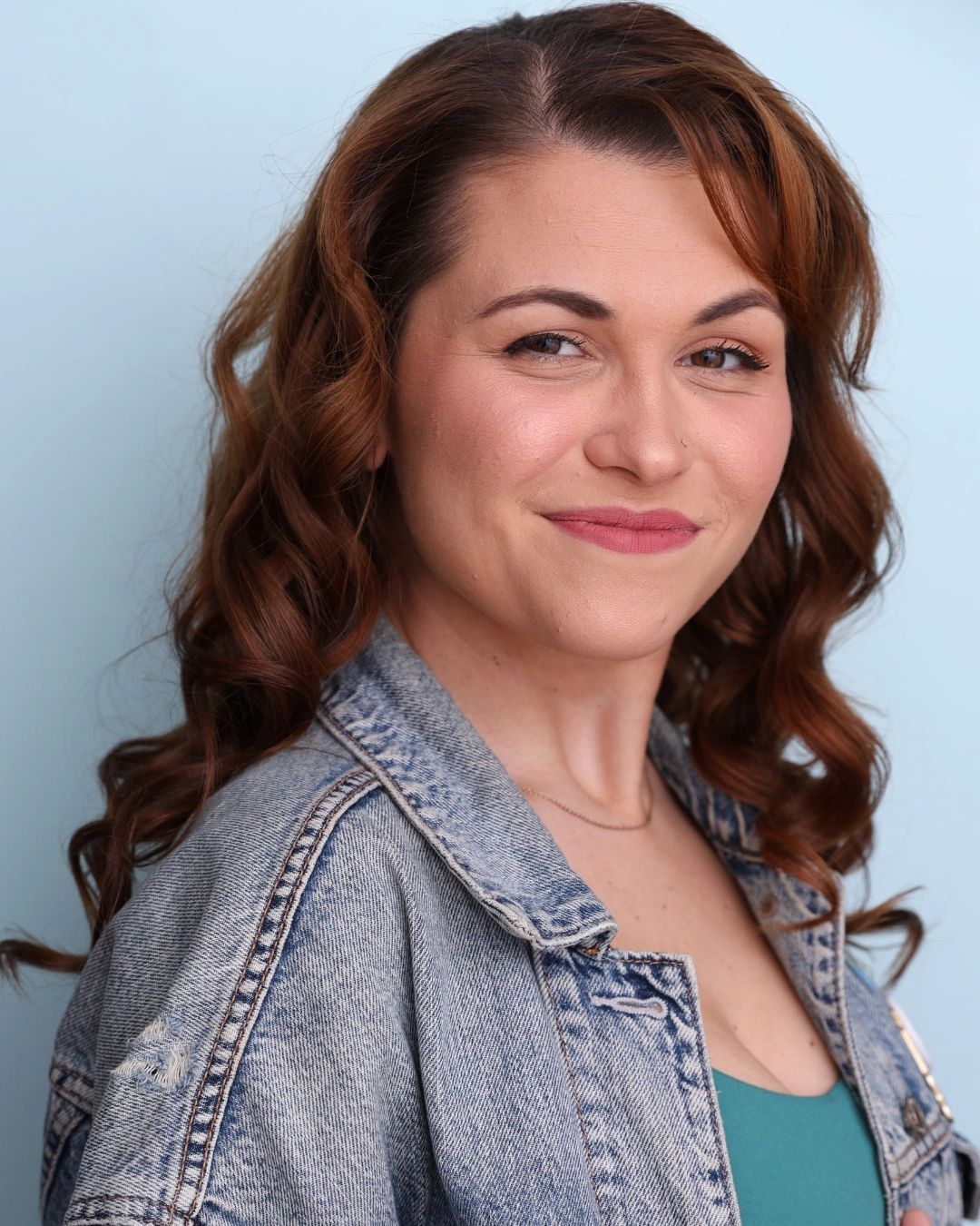 A headshot of Taylor Kellar. She has curled reddish-brown hair and looks at the camera with a smirk.